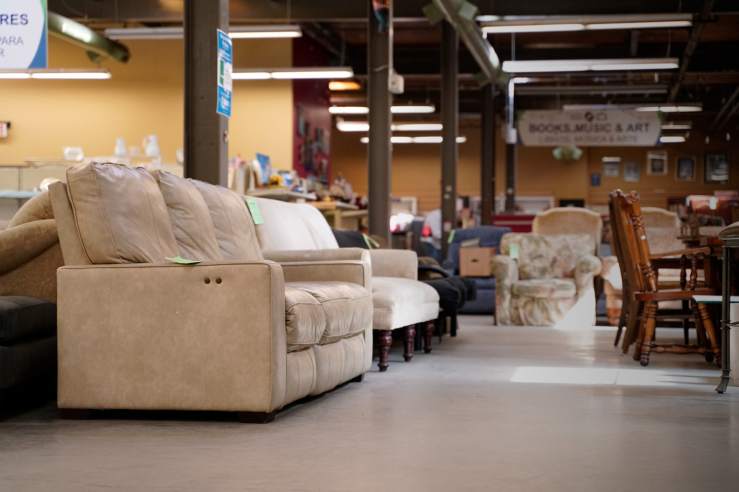 A cream colored leather couch in the Asheville ReStore's upper showroom. Behind it is the bookstore, containing books, music, and art.